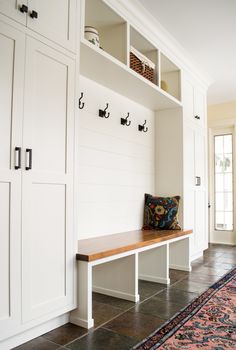 a room with white cabinets and a bench in the center, along with an area rug on the floor