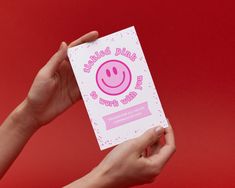 a person holding up a pink card with a smiley face on it