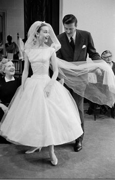 a woman in a wedding dress walking down the aisle next to a man wearing a suit and tie