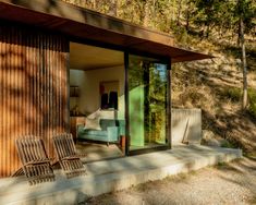 two wooden chairs sitting on the side of a building next to a wooded area with trees in the background