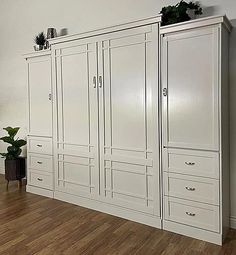 a large white cabinet sitting on top of a hard wood floor next to a potted plant