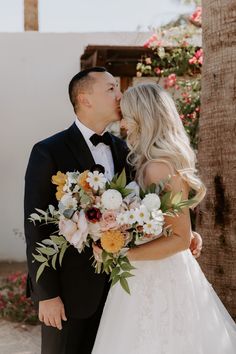 a bride and groom kissing in front of a palm tree