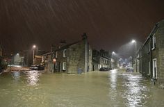 a flooded street at night with cars parked on the side and buildings in the background