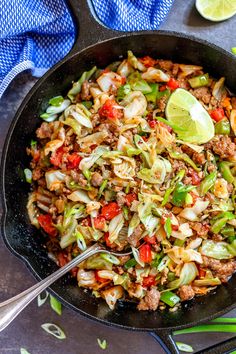 a skillet filled with meat and vegetables on top of a table next to sliced limes