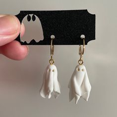 a pair of white ghost earrings is being held up by a person's hand