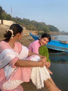 two women sitting on the edge of a body of water