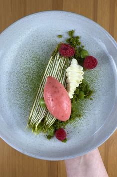 a white plate topped with food on top of a wooden table next to a person's hand