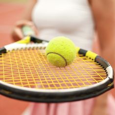 a woman holding a tennis racket with a tennis ball on the top of it