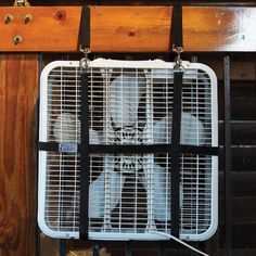 a cat sitting on top of a metal cage in front of a wooden wall with an air conditioner attached to it