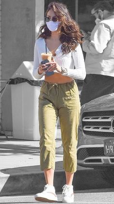 a woman in white shirt and khaki pants walking down street with cell phone