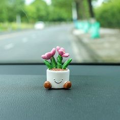 a small potted plant sitting on the dashboard of a car with pink flowers in it