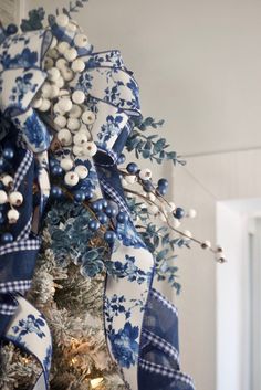 a christmas tree decorated with blue and white ribbon, ornaments and berries on it's branches