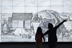 two people are standing in front of a wall with drawings on it and one person is pointing at something