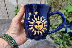 a hand holding a blue coffee mug with a sun and stars painted on the side