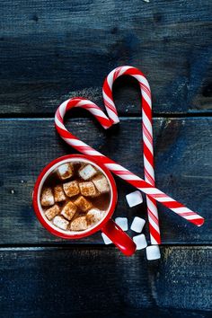 two candy canes are next to a cup of hot chocolate and marshmallows