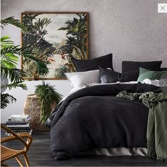 a bed covered in black and green blankets next to a chair with a painting on the wall