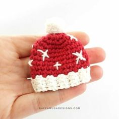 a hand holding a small crocheted red and white hat