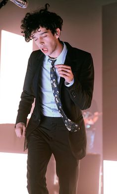 a man wearing a suit and tie standing in front of a light that is shining on him