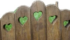 a wooden fence with green hearts cut out of it's sides and grass growing through the holes