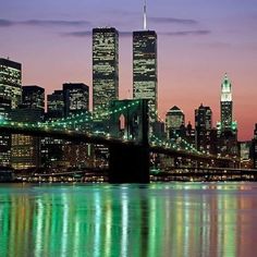 the city skyline is lit up in green and blue at night, as seen from across the water