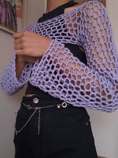 a woman wearing a purple crochet sweater and black pants with her hands on her hips