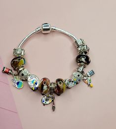 a bracelet with charms on it sitting on top of a pink table next to a wall