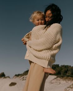 a woman holding a child in her arms on top of a sandy beach next to the ocean