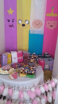 a table topped with cupcakes and desserts next to colorful wall paper decorations