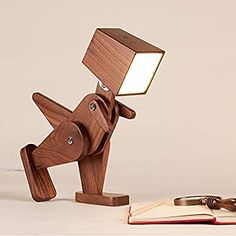 a wooden lamp that is on top of a table next to an open book and pen