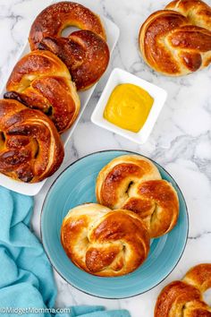 bread rolls on a plate with butter and mustard in the background, next to two bowls of dipping sauce