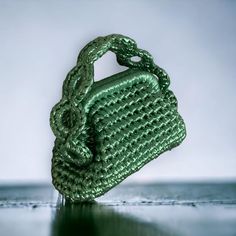 a green handbag sitting on top of a shiny table next to a white wall