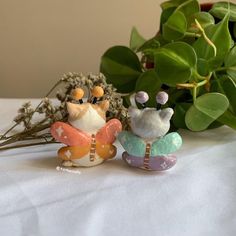 two small figurines sitting on top of a table next to plants and flowers