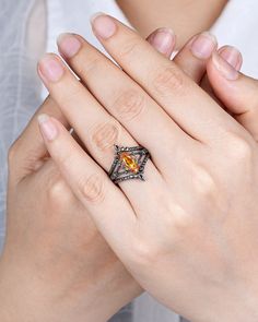 a woman wearing a ring with an orange stone in it's center and surrounded by her hands