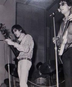 two young men are playing guitars and singing into microphones in an old black and white photo