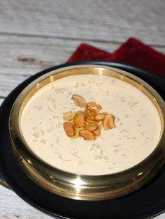 a bowl of soup with nuts in it on a black and gold plate next to a red napkin