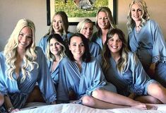 a group of women sitting on top of a bed in matching blue robes and smiling at the camera