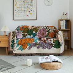 a living room with a couch covered in a floral blanket and coffee cup on the floor