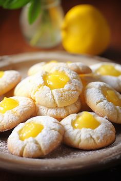 lemon cookies with powdered sugar are on a plate next to some lemons and a vase