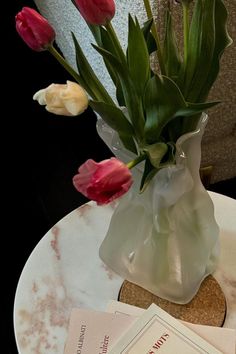 there is a vase with flowers in it sitting on a table next to some papers