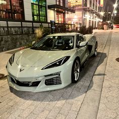 a white sports car parked on the side of a street at night with buildings in the background