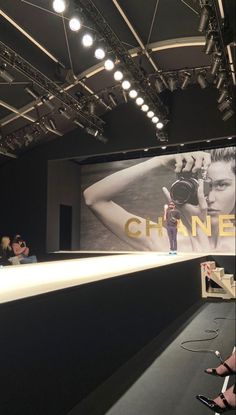 people are sitting in front of a chanel advertisement on the wall at a fashion show