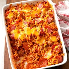 a casserole dish with pepperoni, cheese and noodles in it on a wooden table