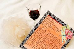 a glass of wine next to an old fashioned letter on a white sheet with flowers