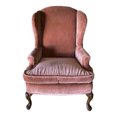 an upholstered pink velvet wingback chair with turned legs and foot rests against a white background