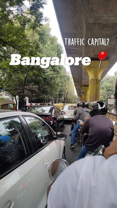 several people riding bikes on the street under a bridge with cars and motorcycles parked underneath it