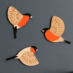 three wooden birds sitting on top of a table next to each other and one bird has an orange breast