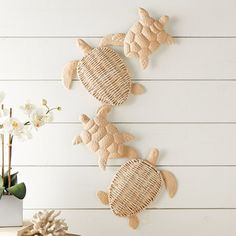 three sea turtle wall hangings on the side of a white wooden wall next to a vase with flowers