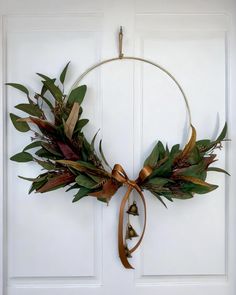 a wreath hanging on the front door with bells and leaves attached to it's sides