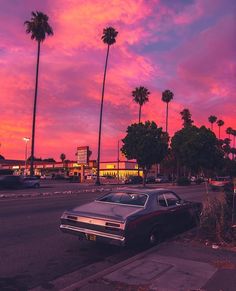 an old car parked on the side of the road in front of some palm trees