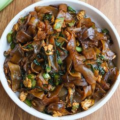 a white bowl filled with meat and vegetables on top of a wooden table next to a fork